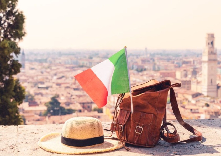 Imagen de una mochila comn la bandera de italia y de fondo unm paisaje de Italia.